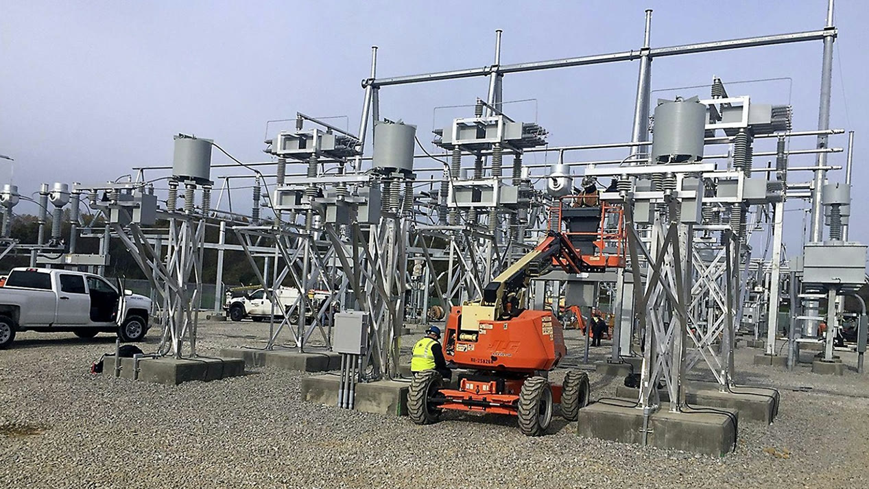 Crew installing switchgear structures at a substation with a boom lift