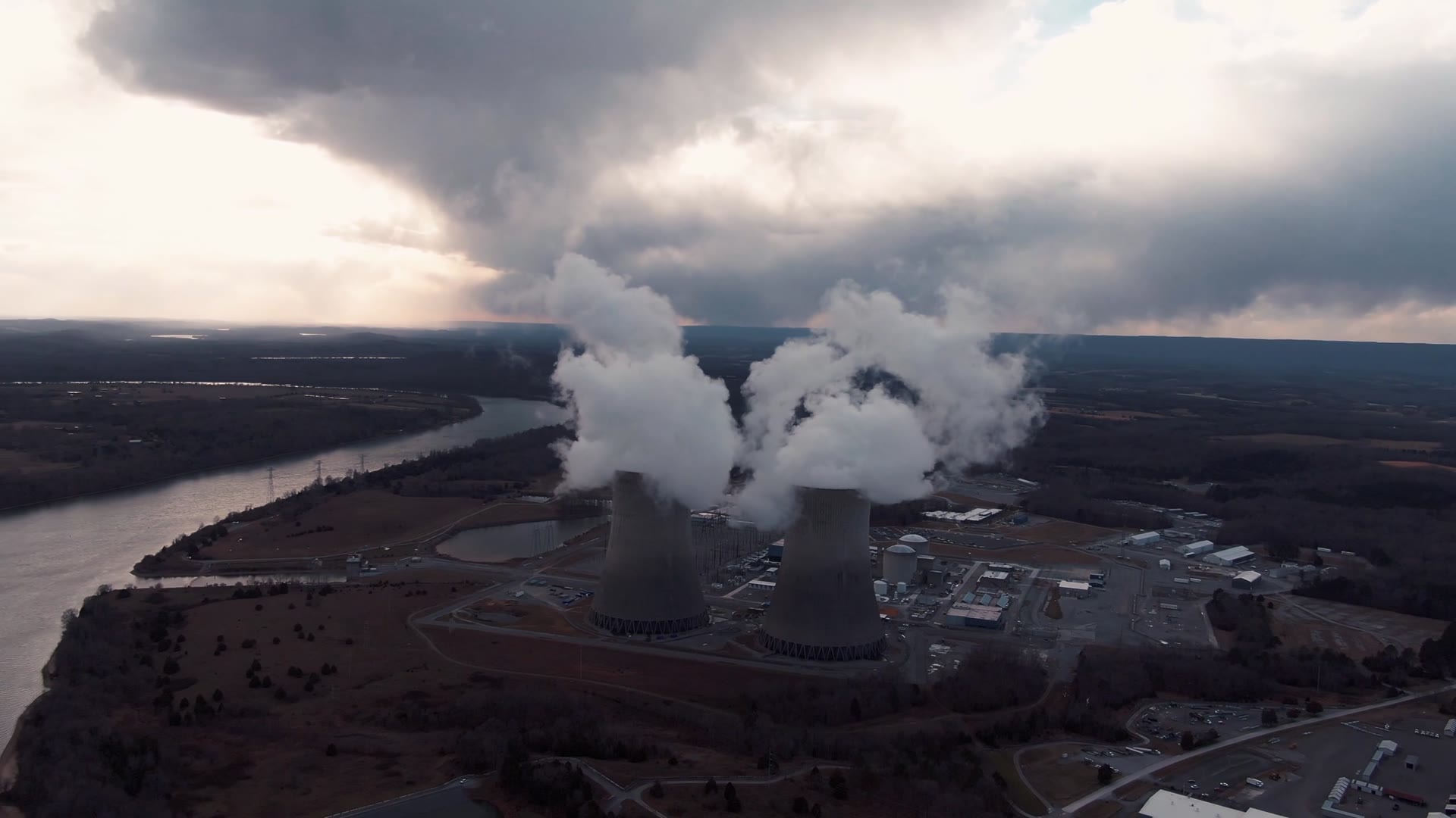 A power station's cooling towers pouring steam under a storm sky, seen from the air