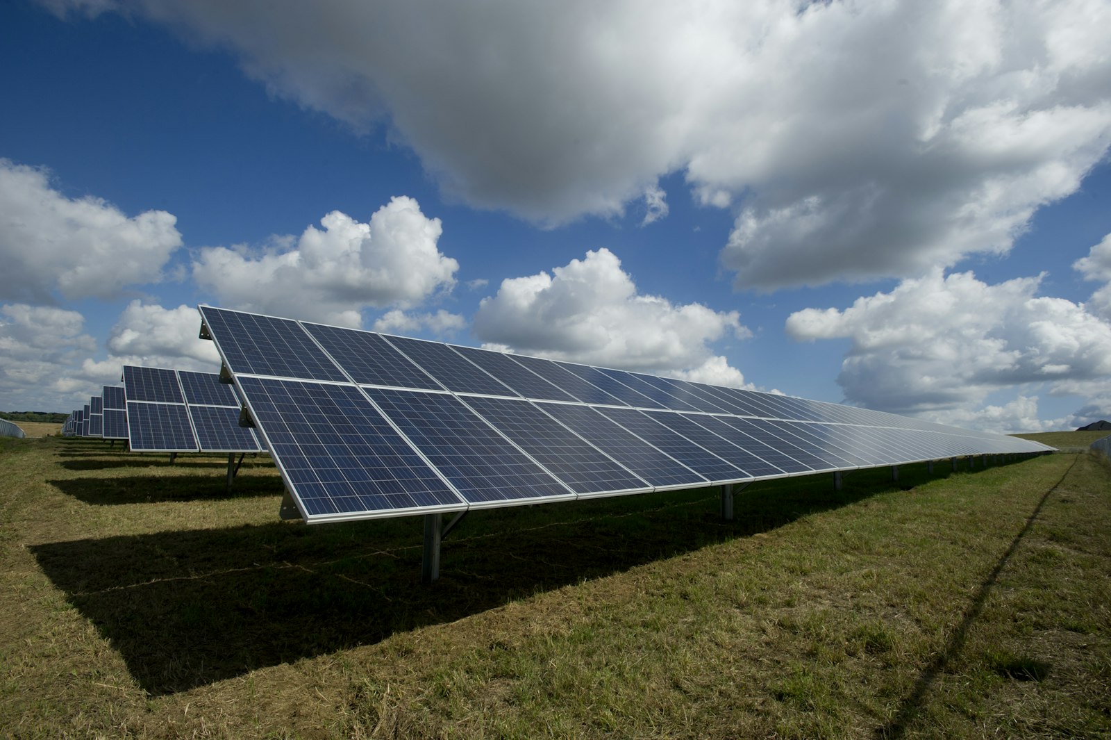 Rows of utility-scale solar panels on a grass field under a partly cloudy sky